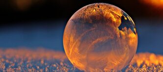 Close-up shot of a frozen bubble with warm reflections resting on a snowy surface at twilight.